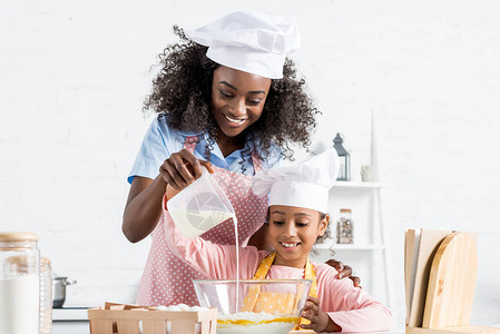 身戴厨帽的非洲母亲和女儿在碗里倒牛奶配图片