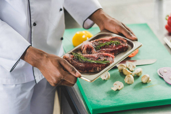 非洲人厨师在餐厅厨房用生肉端着餐盘的图片