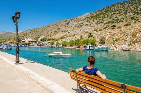 希腊岛之一的小型渔民港口码头坐在长椅上坐着的蓝图片