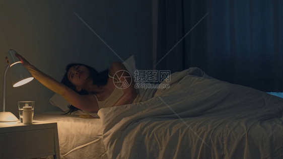 印度女手在深夜在家里的房间里关闭床边的电灯开关图片