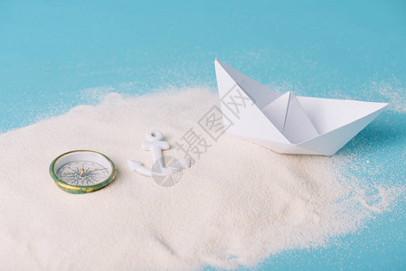 蓝色背景中带纸船指南针和锚的沙子图片