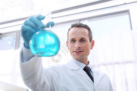 在实验室研究实验室用蓝色液体制成的实验室大衣持有试验管图片
