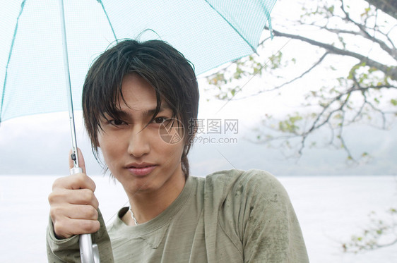 一个年轻的亚洲日本男子在雨天参观天然湖泊和山脉景观并拿着雨伞以防雨的特写肖图片
