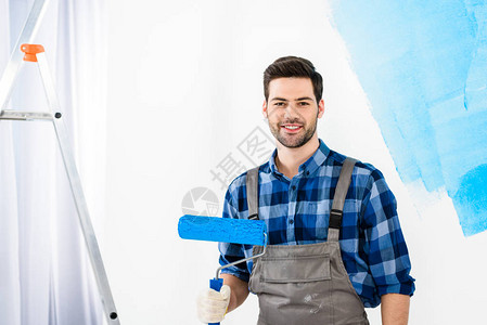 维修工具微笑的男人拿着油漆滚筒刷站着看着相机背景