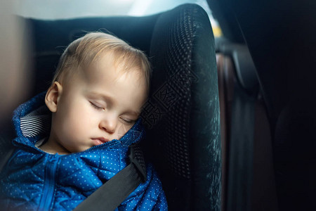 可爱的白种人蹒跚学步的男孩在公路旅行期间睡在汽车的儿童座椅上可爱的婴儿在旅途中在舒适的椅子上睡着了道路上的儿背景图片