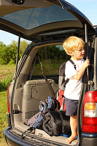 一个年幼的孩子背着包站在他的小型货车后面图片