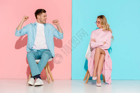 女人对手交叉的不满意男人用紧握拳头欢呼坐在粉红和蓝色图片