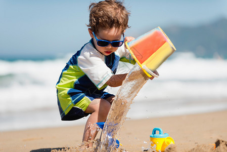 小男孩从沙滩上的桶里倒水图片
