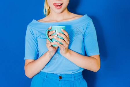 穿着蓝衣服的迷人年轻女孩蓝色杯子握在背景图片