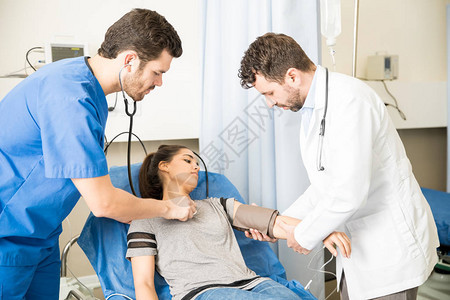 在急诊室检查一名女病人心脏跳动和血压的两名男医图片