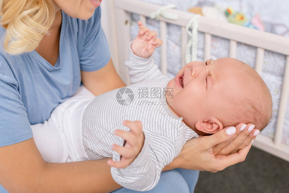 母亲在家中手握着哭泣婴儿图片