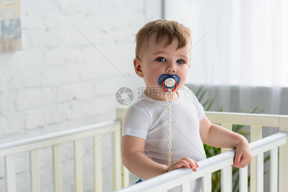 可爱的小可爱男孩用奶嘴在婴儿床看图片