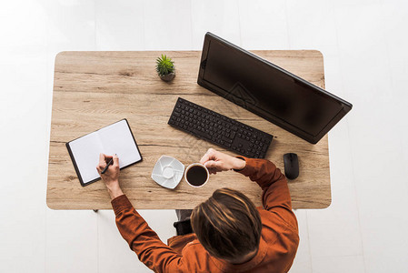 男人喝咖啡在桌子上用盆栽电脑电脑和电脑鼠标写教图片