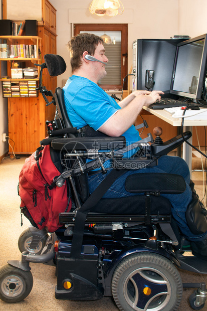坐在多功能轮椅上并使用带有触摸屏幕和无线耳机侧视的计算机的人图片