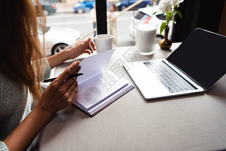 在咖啡馆用笔记本和笔记本电脑与咖啡杯一起在线学习的女图片