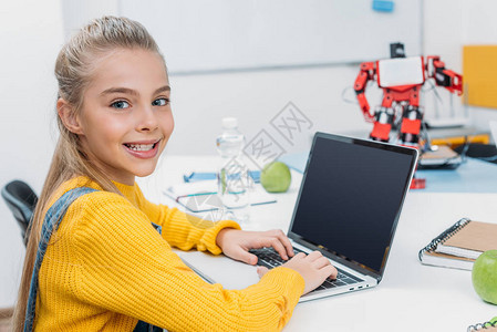 微笑着的女学生坐在有机器人模型的桌边图片