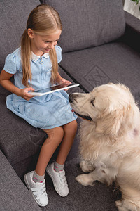 有拉布多犬的快乐幼儿在坐沙发上时使用平板图片