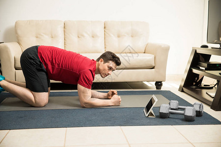 一位年轻男子在家锻炼时观看平板电脑上训练常规的剖面图P图片
