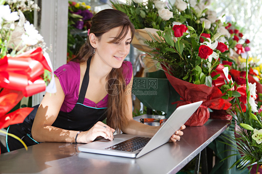 一位有吸引力的花店女老板坐在花店柜台前使用笔记本电脑在线订购库存的肖像图片