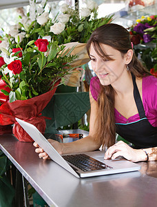 一位有吸引力的花店女老板坐在花店柜台前使用笔记本电脑在线订购库存的肖像图片