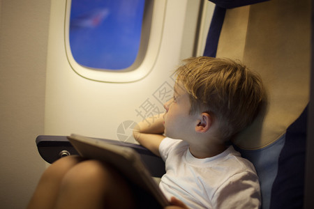 小男孩乘飞机旅行他看着灯光者拿着平图片