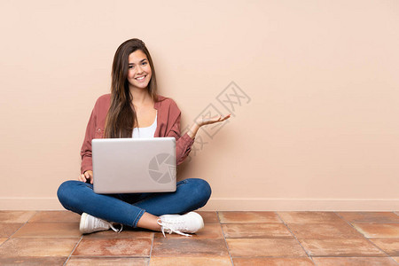 坐在地板上坐着一个手提笔记本手持复制空间的青少年女学生在棕榈上想象图片