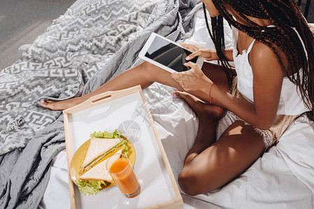 使用平板电脑在床上吃早餐的非裔美背景图片