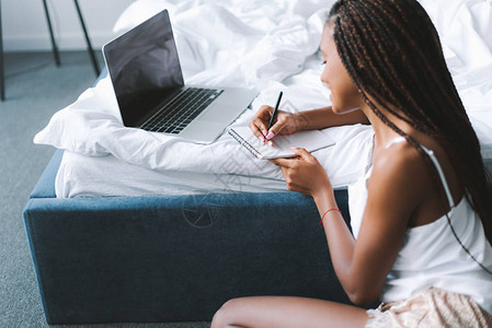 美丽的非洲裔美国女人在床上用笔记本电脑在背景图片
