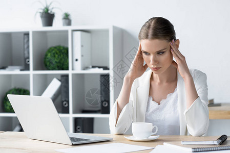 劳累过度头痛的年轻女商人坐在办公室的工作图片