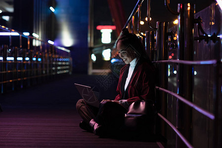 未来之城与喜莫诺的年轻女孩在街上坐着并用笔记本电脑使用图片