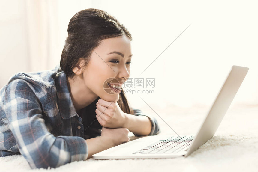 坐在地毯上在家看笔记本电脑监视器的年轻女子近图片