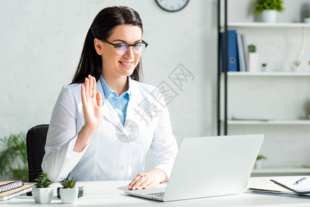 医生在诊所办公室用笔记本电脑与病人进行在线咨询时笑图片