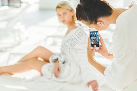 年轻女子用智能手机拍摄她朋友在温泉中心图片