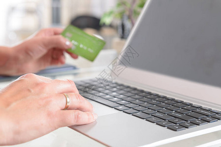 女手持信用卡在笔记本上并用它在线支付电子商务的概图片
