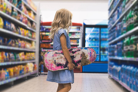 金发孩子滑板在超市架子后图片
