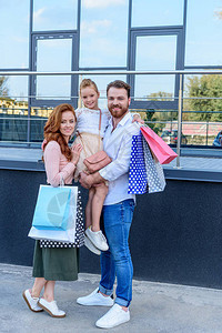 父母和女儿购物后提着购物袋站在街上图片