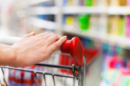 超市手推车上女购物者手的特写图片