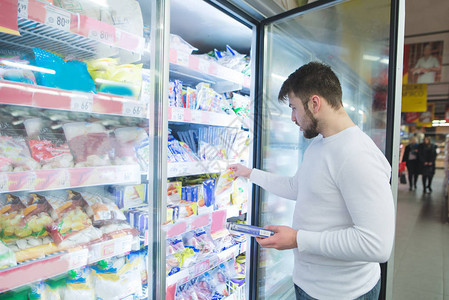 一名男子从超市冰箱的货架上挑选冷冻食品一个人在商店里买产品在图片