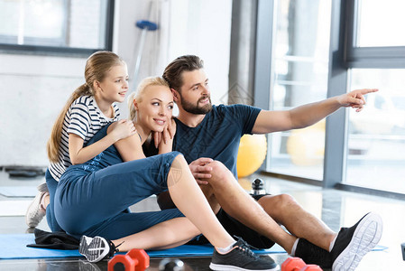 快乐家庭坐在健身馆的垫子上和一个用手展示东西图片