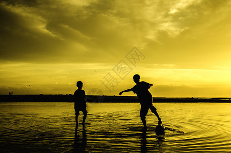 两名男孩在日出时玩海滩足球水和天空模糊不图片