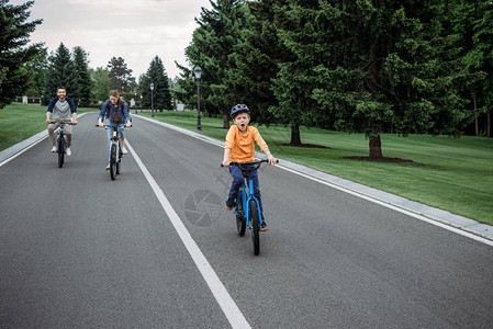 小男孩和父母一起在沥青路上骑自行车图片