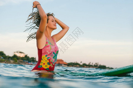 穿着游泳西装的年轻女子在海洋中坐在冲浪板图片