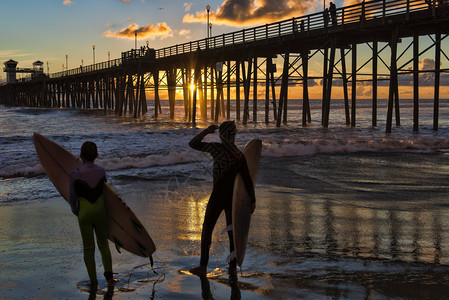 拿着冲浪板的剪影冲浪者在欧申赛德码头观看南加州的日落图片