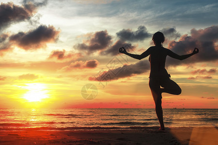 令人惊异的日落时在海滩上做瑜伽姿图片