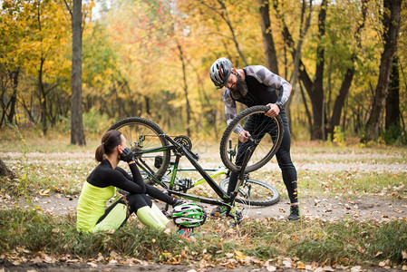 成人男子修自行车而其女友则坐在草地上和图片