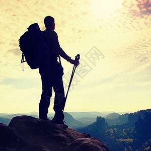 手里拿着大背包和两极的徒步旅行者的剪影在落基山脉的阳光多彩黎明人站在迷雾笼罩的山谷上方图片
