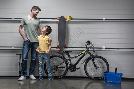 微笑的父亲和儿子站在手持自行车和滑板的车图片