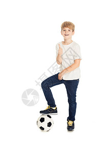 笑的可爱男孩把腿放在足球上举起拇指在图片