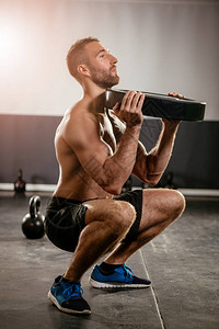 年轻的肌肉男用哑铃做蹲下运动强壮的男图片