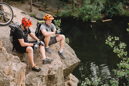 坐在森林中河流附近岩石悬崖上运动水瓶子的背囊朋友骑自行车者图片